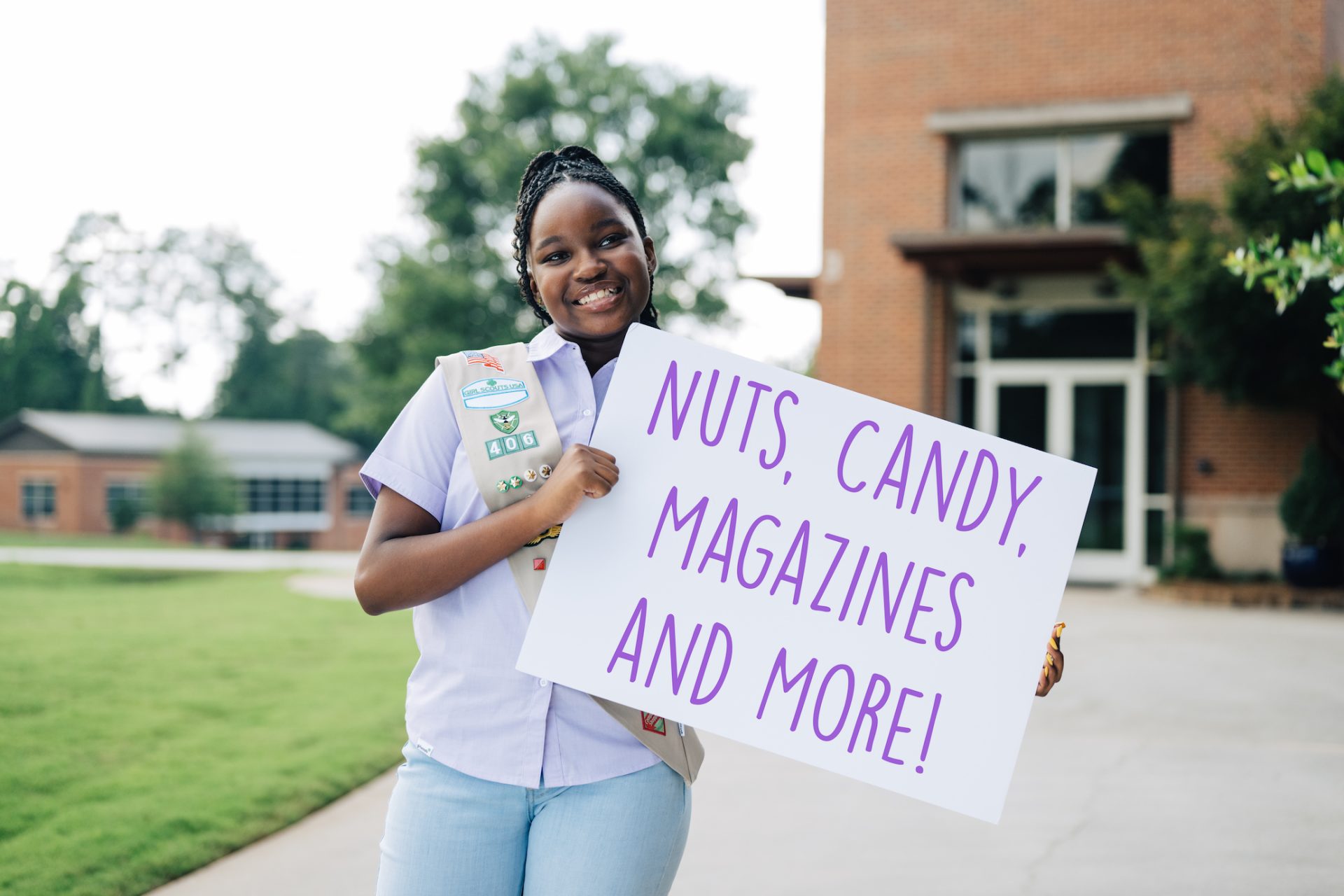 Cadette Girl holding a sign that reads "Nuts, Candy, Magazines, and More"!